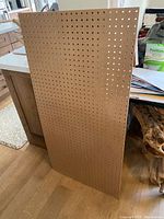 Photo of standing beige peg board with multiple evenly spaced holes on the surface.