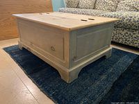 Solid rectangular pine coffee table with panel sides and hollow base, shown closed on a dark rug next to a patterned sofa.