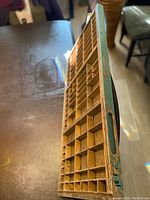 Angled close-up of the wooden printer's tray showing many small compartments and worn paint on edge