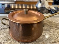 Small round copper pot with lid placed on countertop, showing patina and tarnish.