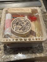 Top view of the 6-piece master artist survival kit showing the brush cleaner container, hand soap stick, and plastic wrapped items inside the beige brush cleaning basin.