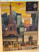 Photo of the unopened 1000-piece jigsaw puzzle box showing a Paris cityscape with Eiffel Tower and other landmarks under a yellow sky.