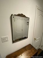 Vintage console mirror hung on wall above wooden console table, showing floral etching and detailed faux wood embossed frame.