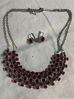 Full view of the necklace and earrings showing red stones set in silver-tone metal with chain closure and lever-back earrings.