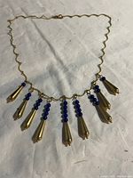 Full view of the gold-tone metal necklace with blue bead and teardrop pendants laid on a cloth background.