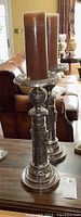 Pair of ornate silver tone metal candlesticks with brown pillar candles placed on a wooden surface