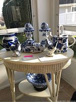 Table display of all ceramic items including vase, watering can, hens, candlesticks, cat figurine, and bowl with stands in a sunroom setting.