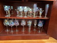 Full set of assorted crystal stemware with iridescent finish inside wooden cabinet.