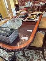 Close-up image showing the dark polished wood dining table with a carved edge and various items placed on top.