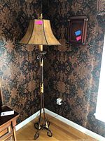 Full view of floor lamp showing metal base, gold decorative details, and beige lampshade alongside wall-mounted key cabinet with closed glass door.