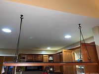 Wide view of wooden hanging shelf suspended by two black metal rods attached to ceiling mounts, positioned over kitchen area.