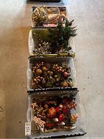 Overview of four plastic bins filled with assorted holiday decorations including faux florals and figurines