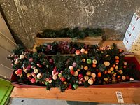 Holiday garlands with faux fruit laid out in a box showing variety of fruit types and greenery
