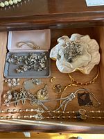 Drawer with costume jewelry containing necklaces, earrings, bracelets laid out along with fabric-lined trinket containers holding other jewelry pieces