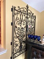 Two hinged metal gate panels leaning against wall with blue glassware at bottom