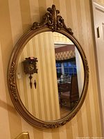 Mirror hanging on striped wallpapered wall showing its full oval shape with ornate detailing on frame.