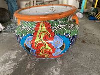 Angled side view showing colorful traditional Mexican floral ceramic painting with orange rim and handles on planter.