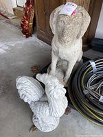 Full view showing both the rooster and dog cement sculptures side by side on a concrete floor.