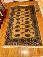 Full top view of the hand-knotted wool rug laid on wooden floor showing the beige field with rows of dark medallions and detailed border
