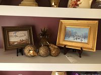 All items arranged on a shelf: two framed prints on stands, glass pineapple, three glitter pears