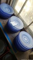 Stacks of blue glass plates with spiral designs photographed on a windowsill, showing multiple plates in three stacks.