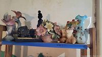 Several ceramic and coal items arranged on a wooden shelf including bird figurines, coal sculpture, flower basket, animal figurines, and vase