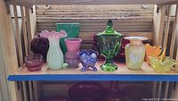 Full view of all nine colored glass items including vases and bowls on wooden shelf