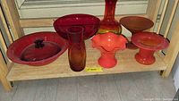 Shelf with eight colored glass items including vases, bowls, a covered bowl, and stemware in red and amber colors.