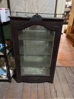Front view of the dark wooden display cabinet with glass front, decorative carved top, and metal railing.