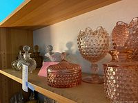 Shelf display of hobnail Duncan glassware including covered dishes and perfume bottles.
