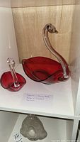 Pair of Duncan Miller swan-shaped bowls with ruby red bases and clear glass necks and heads inside a light wood display case.