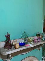 Shelf view of nine assorted Fenton glass pieces against turquoise wall
