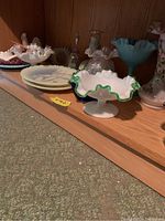 Shelf view showing milk glass green crest bowl alongside hand painted floral plates and dishes