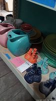 Two Fiesta ceramic pitchers, one turquoise and one pink, displayed on shelf