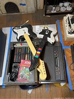 Atari 2600 console with open compartment showing game cartridges and three guitar controllers laid on top.