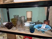 Wide view of glass and china vases, bowls and dishes on shelf showing variety in colors and styles