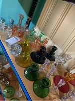 Wide view of multiple pairs of colored and clear glass candle holders arranged on shelves, showing variety of colors and designs.