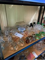 Shelving display of multiple clear and colored glass candle holders, showcasing variety in design and color.