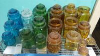 Overview of multiple colored glass L.E. Smith canisters on metal shelving, showing 15 jars in blues, greens, ambers, and clear glass.