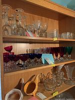 Three-tier wooden shelf displaying colored stemware grouped by color