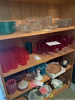 Shelving unit with multiple shelves showing stacks of aqua plates, clear cups and saucers, ruby red and gypsy fire tumblers, ruby red stemmed goblets, various decorative bowls and candy dishes in ruby and aqua colors.