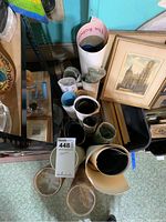 Rolled posters and prints bundled together, some in protective plastic, next to framed prints and other miscellaneous items.