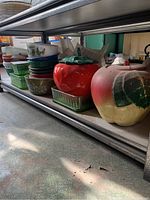 Bottom shelf view showing ceramic fruit cookie jars, nested Pyrex bowls, printed bowls and green glass dishes