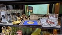Photo showing various glassware including railroad-themed glasses, framed anniversary coin in blue background, ashtrays and other glass items on shelves.