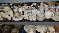 Shelves filled with multiple porcelain tea sets, cups, saucers, plates, teapots in floral and gold-accented designs.