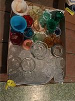 Overhead photo of entire lot showing various colorful glass shot glasses, toothpick holders, and small cream and sugar containers laid out in a cardboard box.