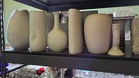 Shelf showing various vases in white and cream colors with embossed floral and geometric patterns.