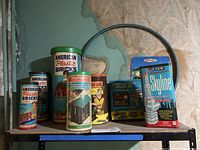 Multiple vintage building toy sets displayed on a metal shelf with three American Plastic Bricks tins, Lincoln Logs tin, Builder and Panel set, and Skyline construction set.