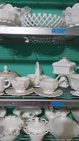 Three shelves filled with a variety of white milk glass items including bowls, baskets with lattice edges, and covered dishes.
