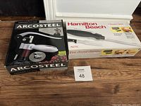 Photo of boxed ArcoSteel corkscrew and Hamilton Beach electric carving tool side by side on floor.